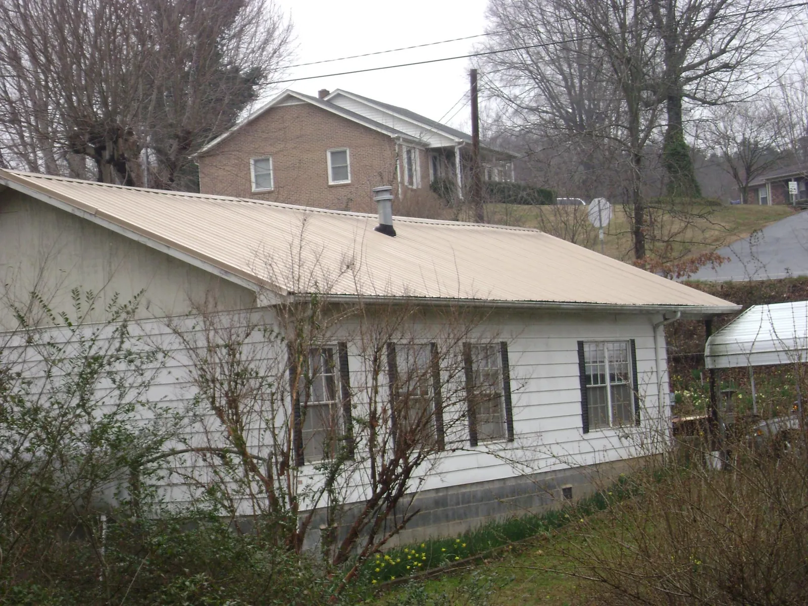 Tan metal roof on a white sided house set into a hillside — Commercial Roofing by Roofing Brothers in Viola